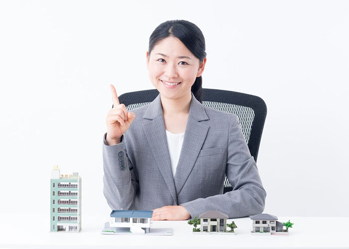指を立てる女性と机に置かれた家の模型